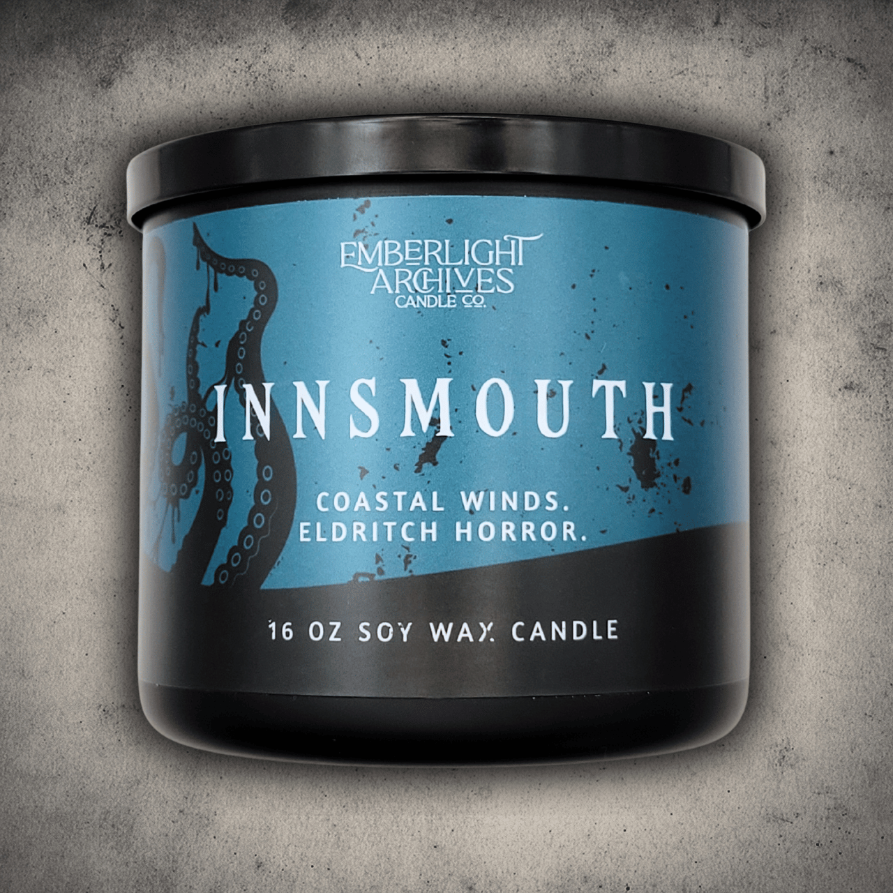 Emberlight Archives Innsmouth candle in a 16oz black glass jar with blue tentacles label against a gray stone background, Coastal Winds and Black Coral scent.